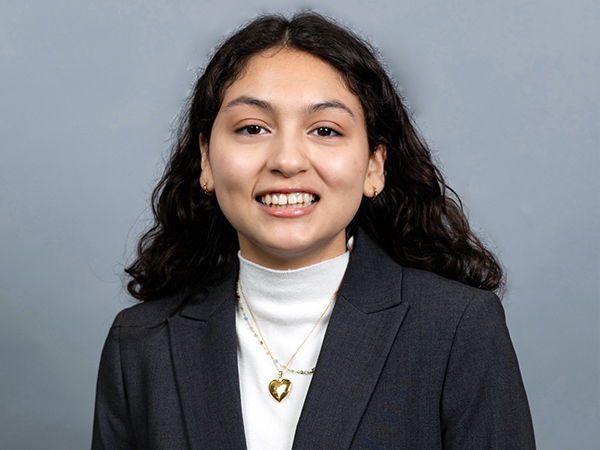Headshot of a smiling student wearing a white turtleneck and a dark blazer