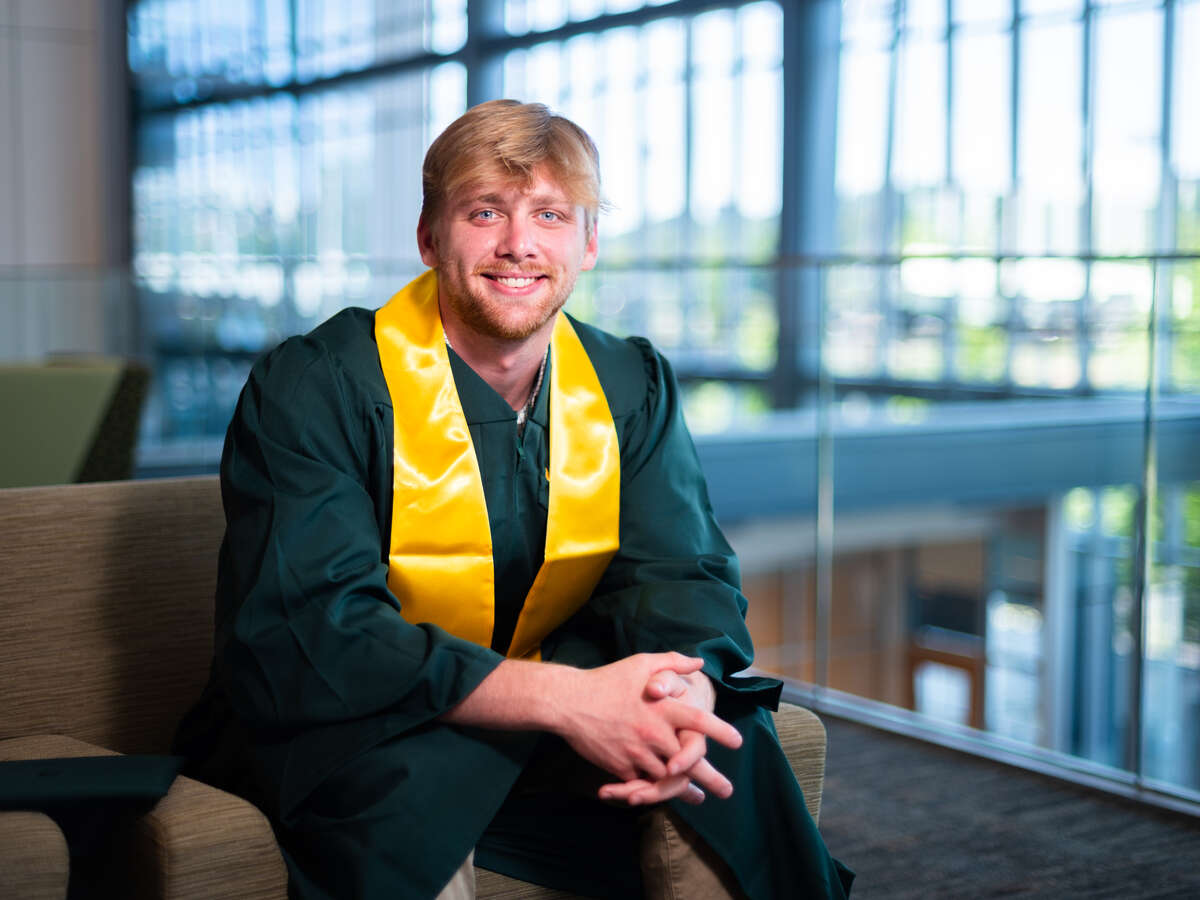 Smiling student with blonde hair wearing a green graduation robe and gold stole