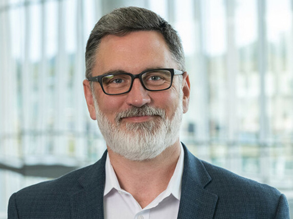 Man with short brown hair and a white beard wearing glasses and a navy blue blazer