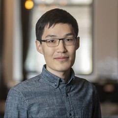 An Asian male with short black hair wearing glasses and a gray button-up shirt.