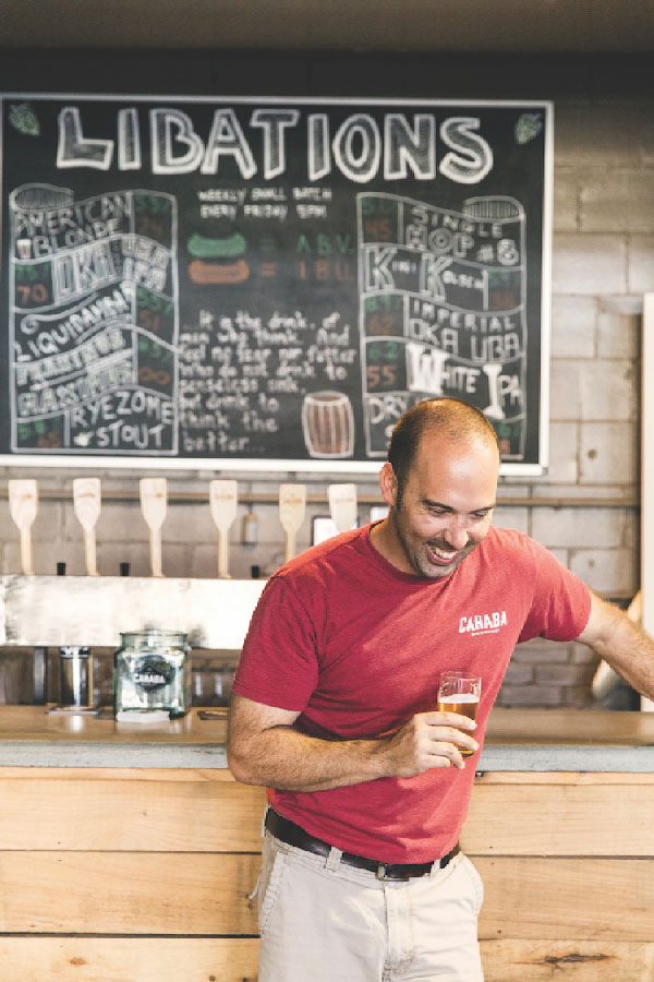 Eric Meyer at Cahaba Brewing in front of a blackbaord showing their day's beer offerings. 