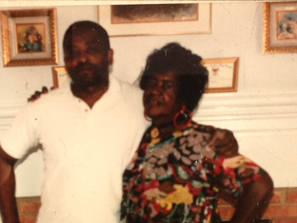 Vintage picture of James and Ollie hurt, at home in front of framed pictures, arms around their shoulders.