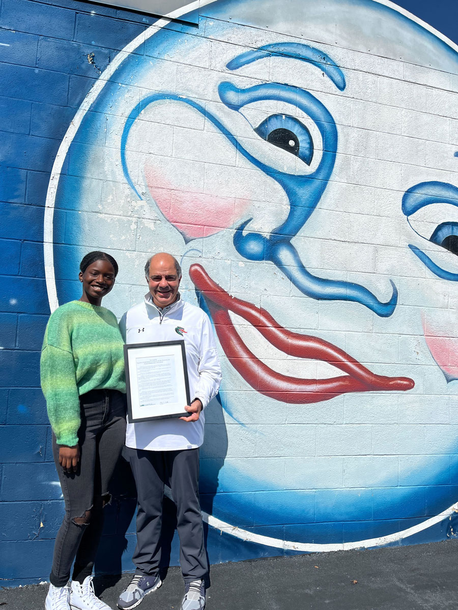 Niki Ookeditse and Joe Maluff standing in front of a large Full Moon logo mural (moon with a smiling face).