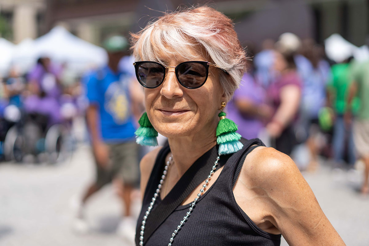 A middle-aged woman in black sunglasses and a sleeveless shirt, with white and red hair.