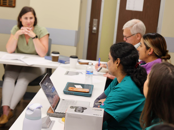 Image of several people talking at a table in a meeting setting with a laptop open on the table 