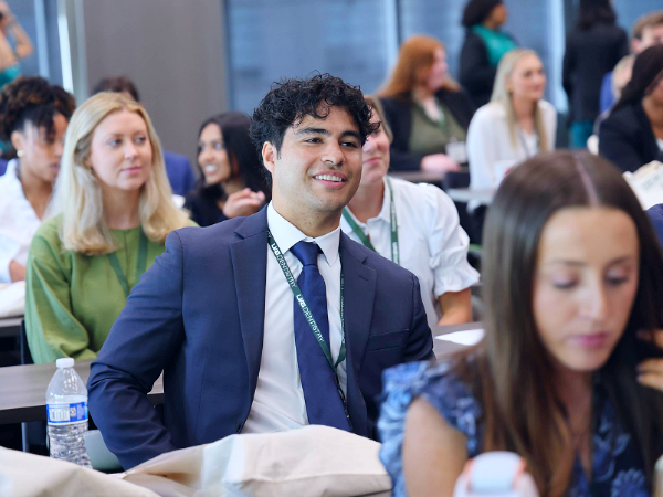 Man with brown hair and blue suit with green lanyard reading "UAB Dentistry" smiling candidly among other sitting in a conference setting