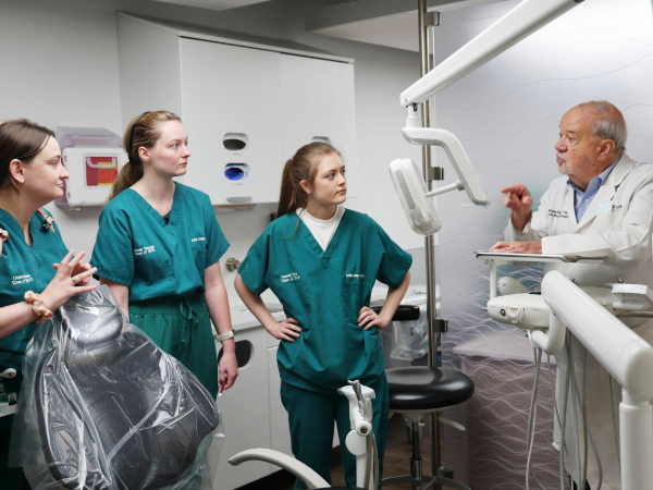 Three dental students looking at talking faculty member in clinic