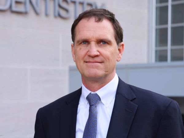Jon Bowie, a man in professional attire smiling for photo in front of concrete building outdoors