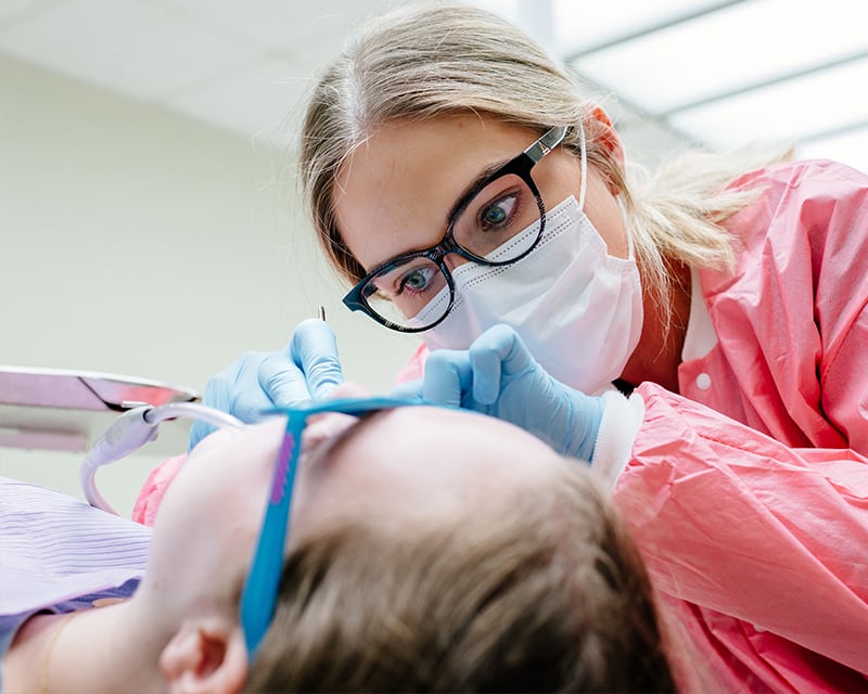 Woman in surgical mask examining the mouth of a young patient.