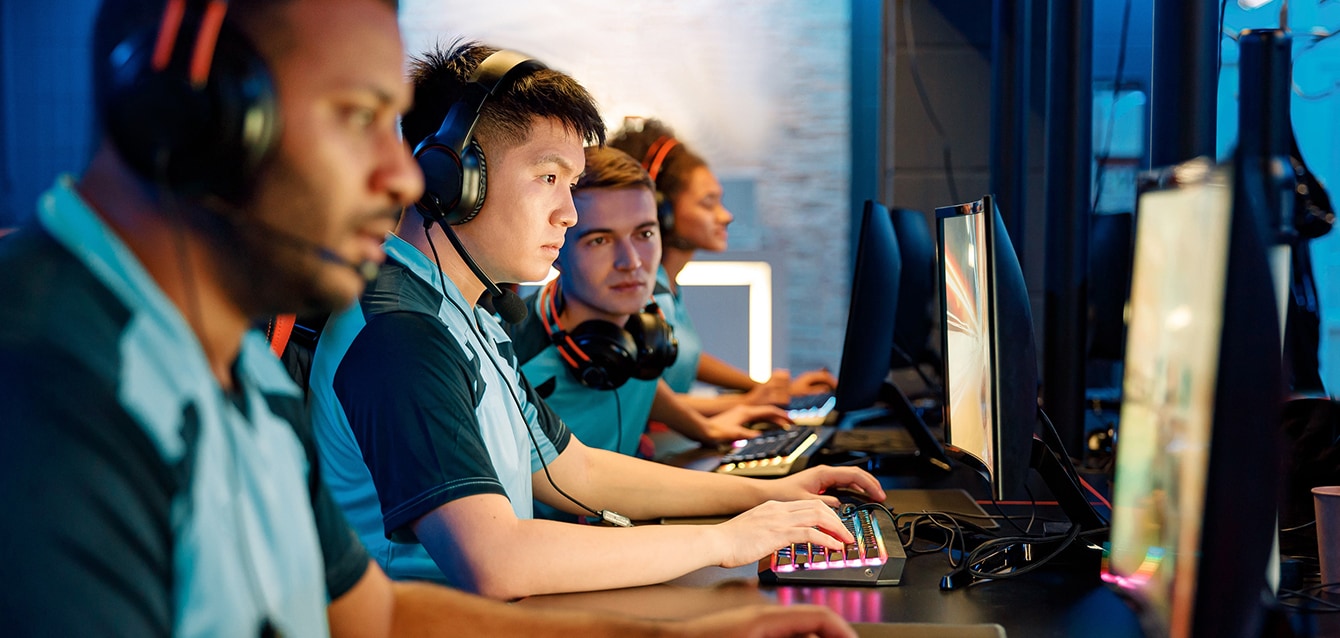 A diverse group of young men and women sit in front of screens, wearing blue team polos and headsets.
