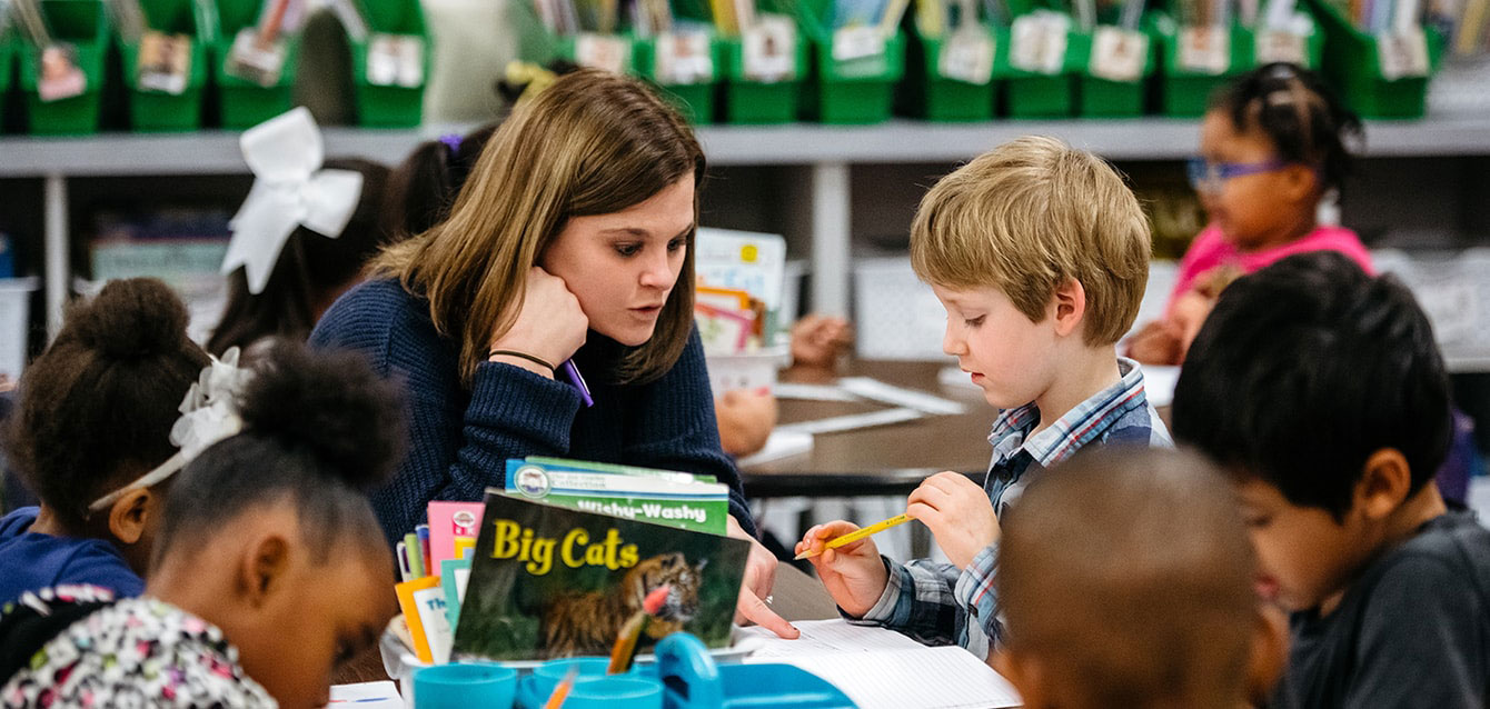 A student teacher works with elementary school children in their classroom.