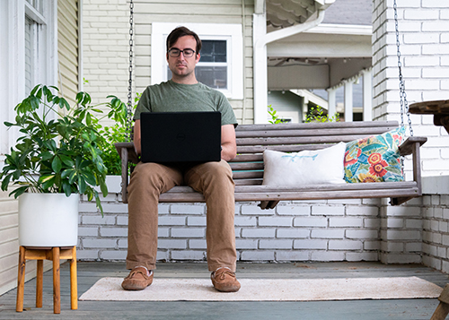 Photo of man working on his laptop while seated on his front porch