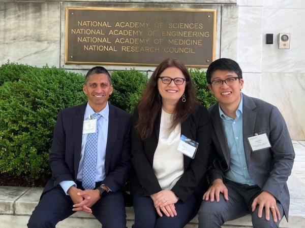 Three people pose in front of the National Academies building