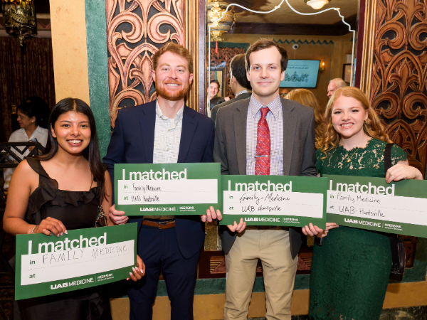 Four well-dressed people hold green UAB signs showing that they matched into family medicine. 