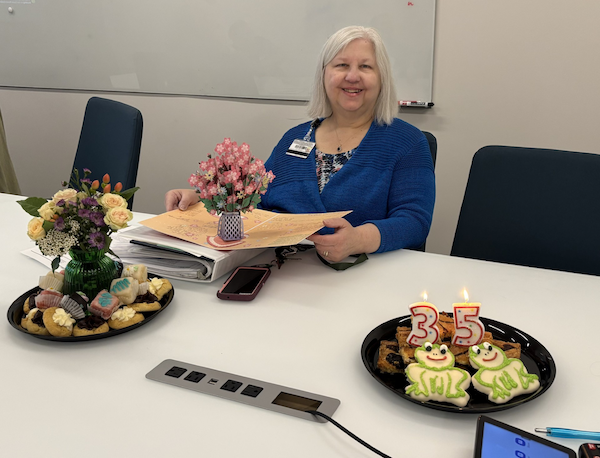 Denise Coston sitting at a table with celebratory treats and a pop-up card that opens to a flower bouquet.