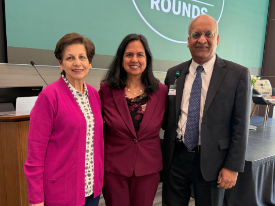 Mona, Fouad, M.D., MPH, Sharmila Makhija, M.D., MBA, and Anupam Agarwal, M.D., stand in front of a large green graphic behind them displays "Heersink Grand Rounds" in white text with a white torch and a white circle.
