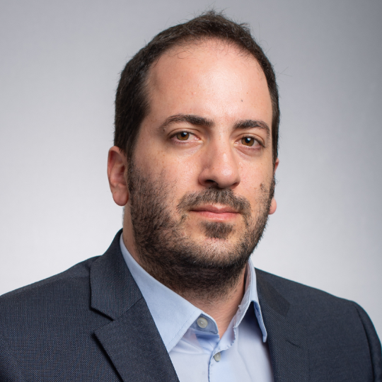 Professional headshot of Massimo Fazio, Ph.D., wearing a dark suit and blue dress shirt.