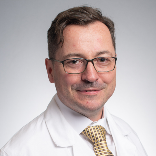 Professional headshot of Rafael Grytz, Ph.D., wearing glasses, a white lab coat, and striped tie.