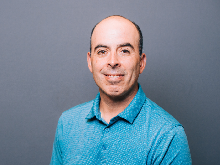 Carlos Orihuela, Ph.D., wears a blue shirt in front of a gray background.