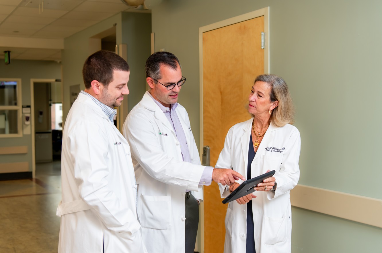 three abdominal radiologists in white coats reviewing imaging on an tablet in the hallway of the hospital