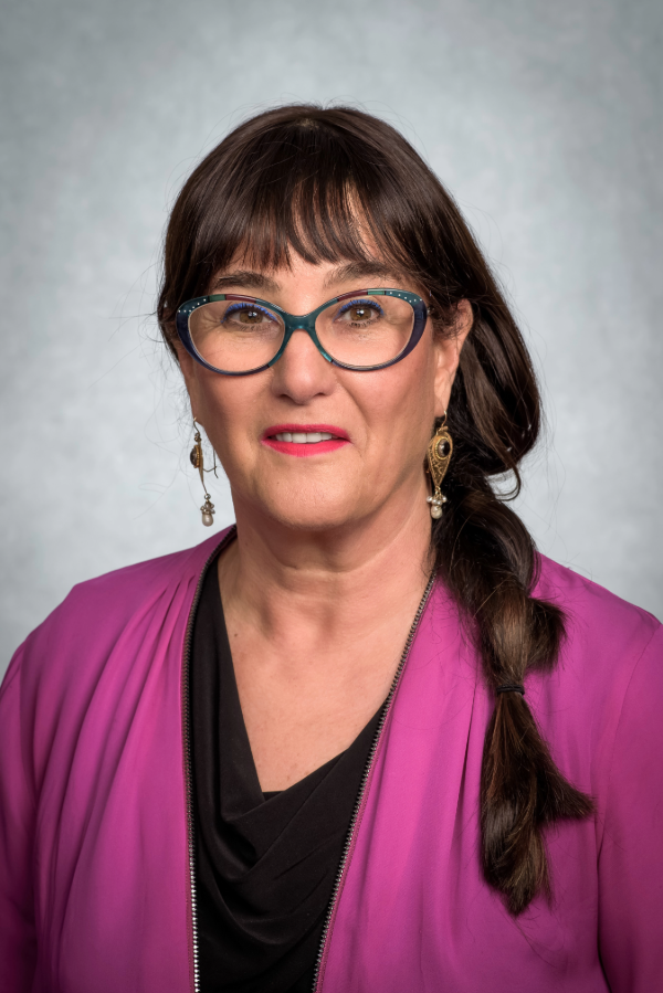 Ronit Elk, Ph.D., stands in front of a gray background.