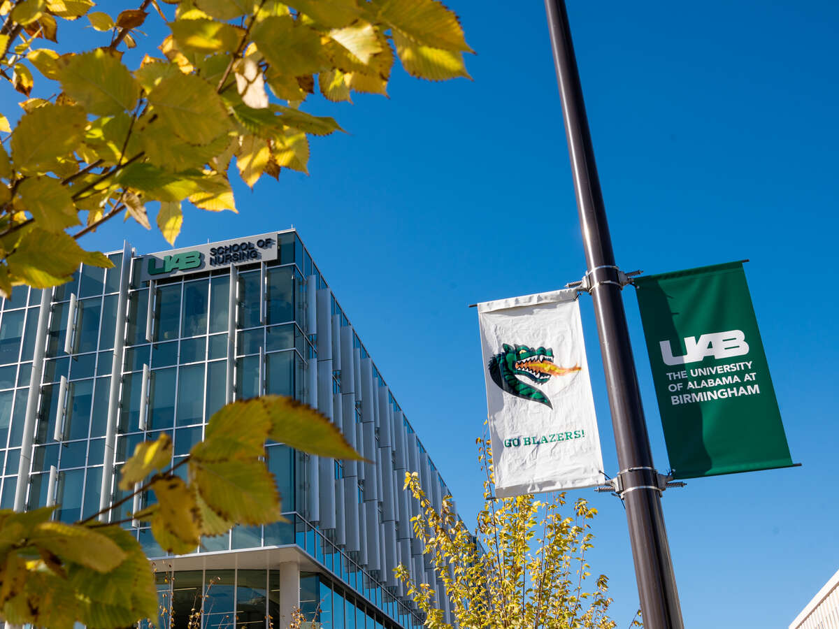 Exterior of the School or Nursing with tree in yellow fall color and UAB banners on light pole in foreground, October 2023.