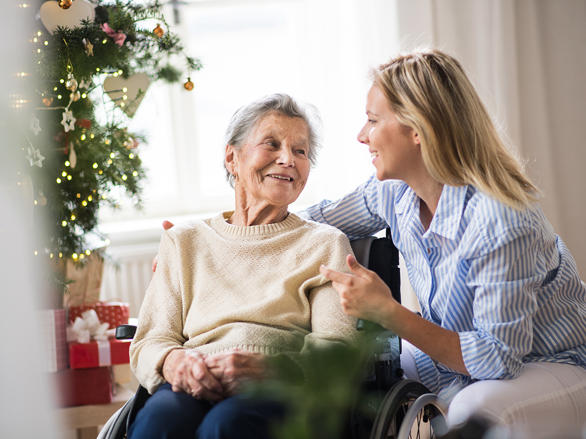 A senior woman in wheelchair with a health visitor at home at Christmas time, talking.