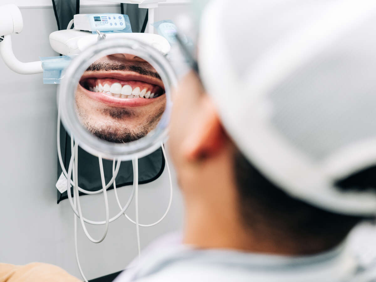 Photo of man smiling in a mirror, looking at his teeth in the UAB Dentistry Clinic.