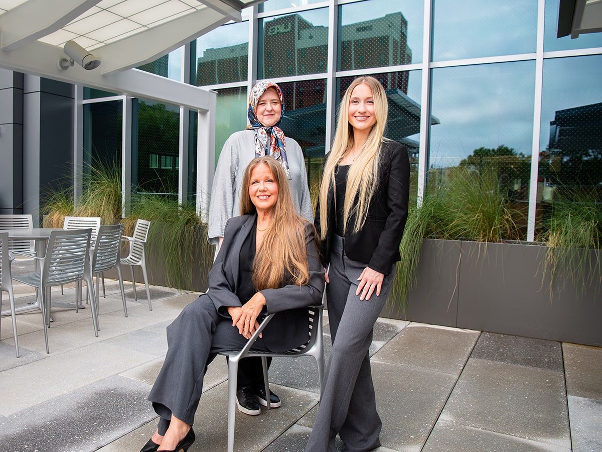 Two women standing behind a woman sitting on a chair.