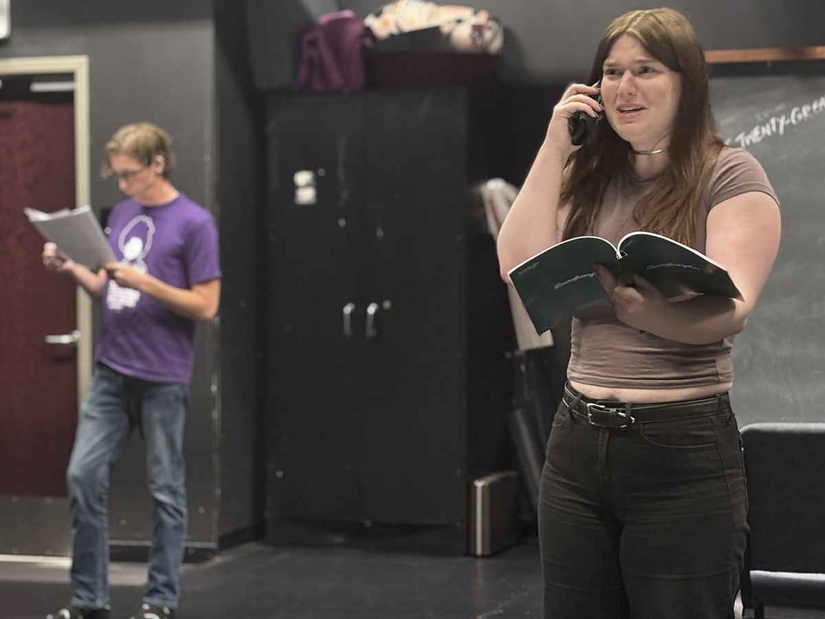 A student holds a phone and a script, with another student in the background, during rehearsals for "Red Flags" in the UAB Acting Studio. 