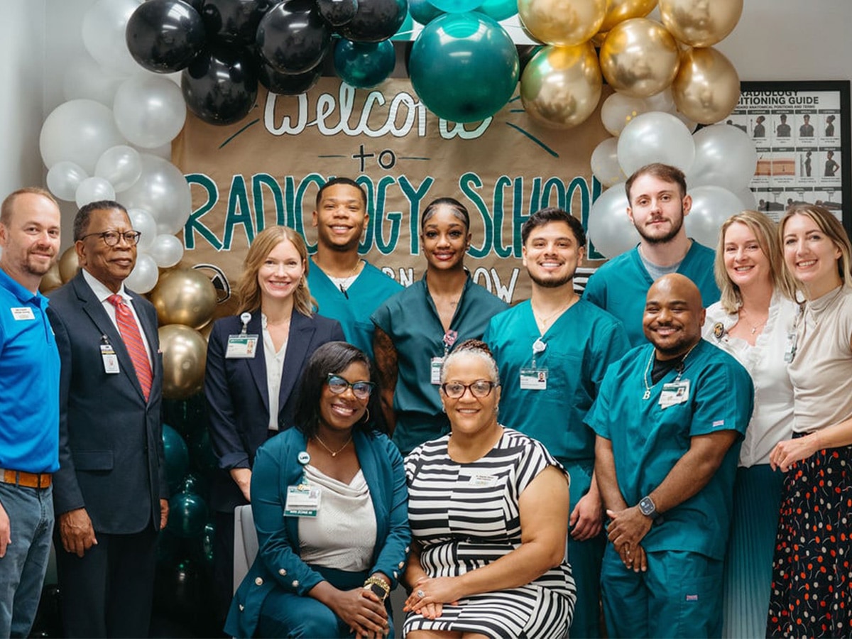 Group of people posing in front of a “Welcome to Radiography School” sign and balloon display at a radiography program welcome event.