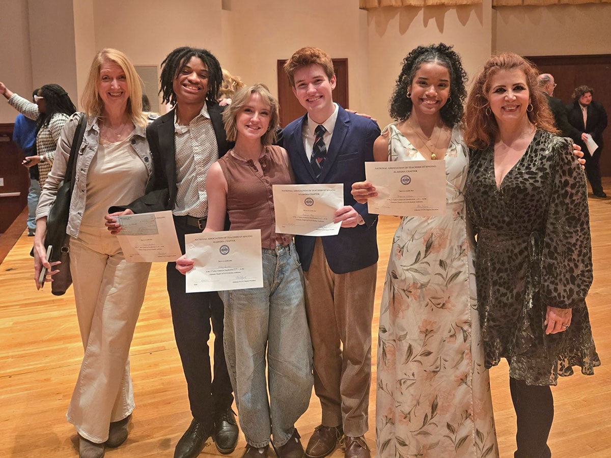 Students pose on stage with their teachers and their awards after winning student singing competitions.