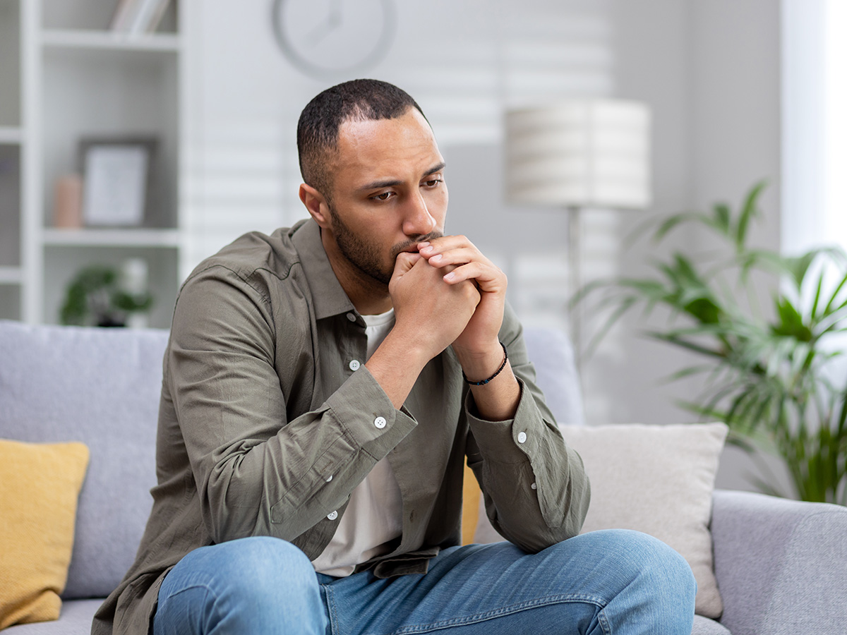 Man sits solemnly on gray couch.