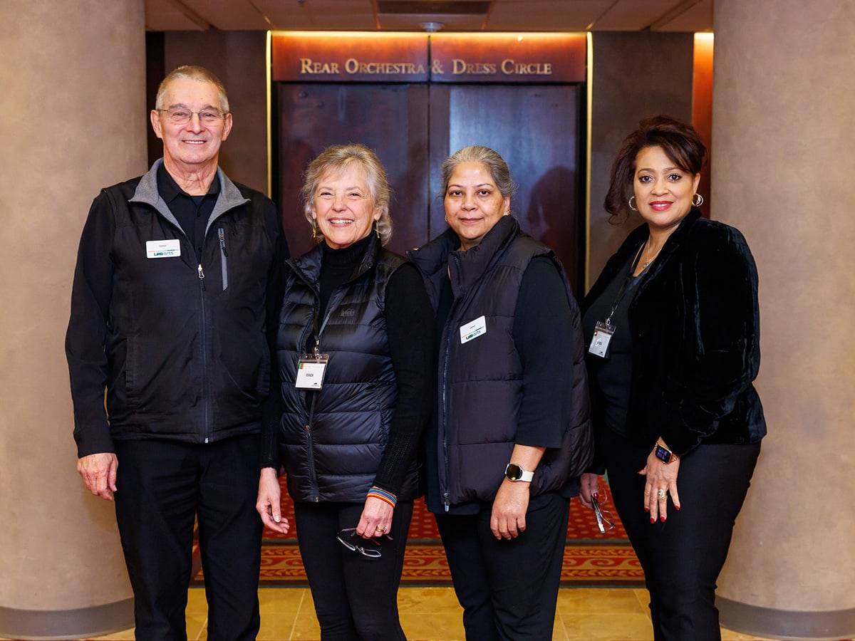 Volunteers dressed in all black so they do not interfere with performances pose together and smile, standing outside the Jemison Concert Hall.