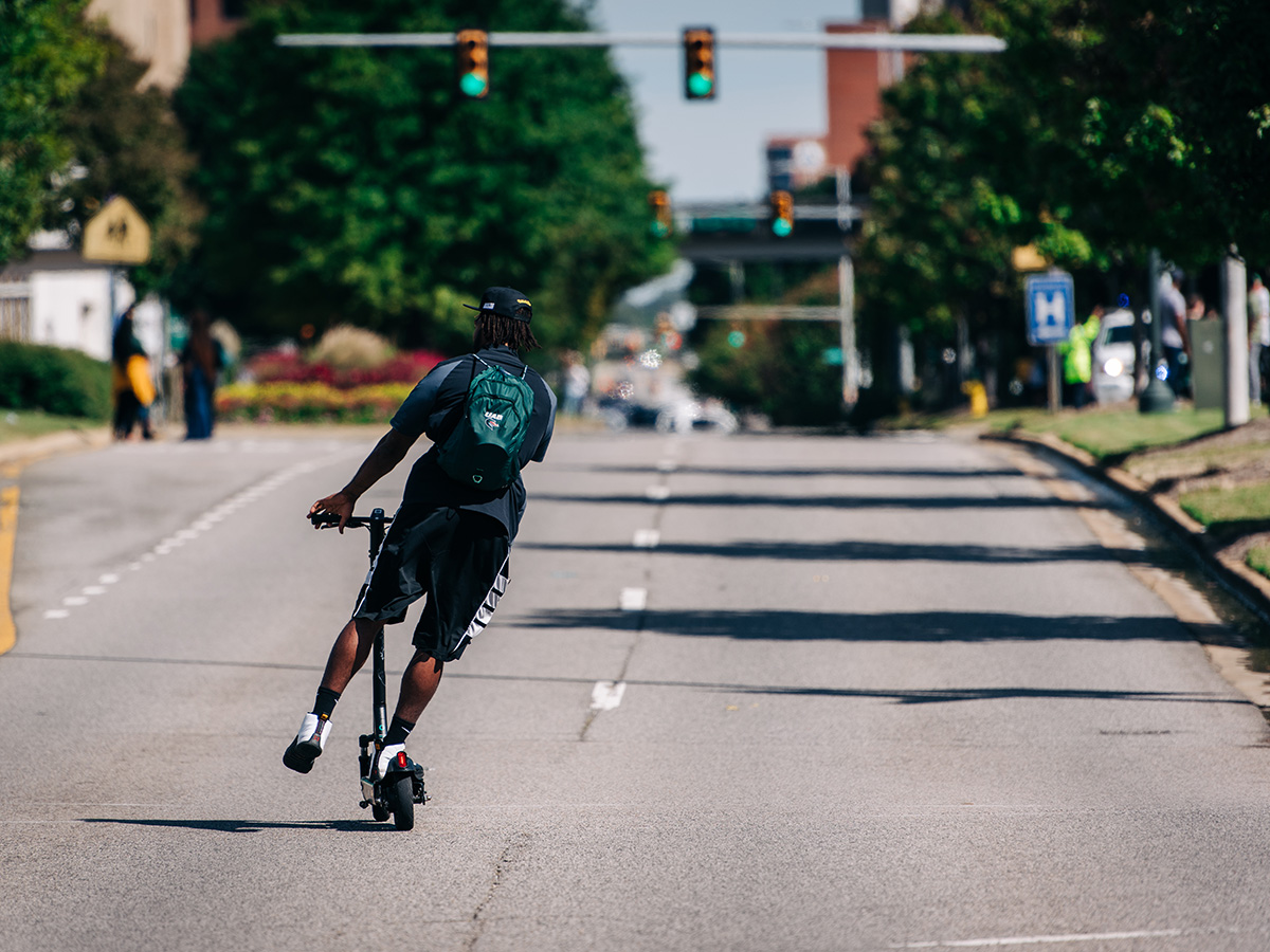 A student riding a manual scooter down University Boulevard.