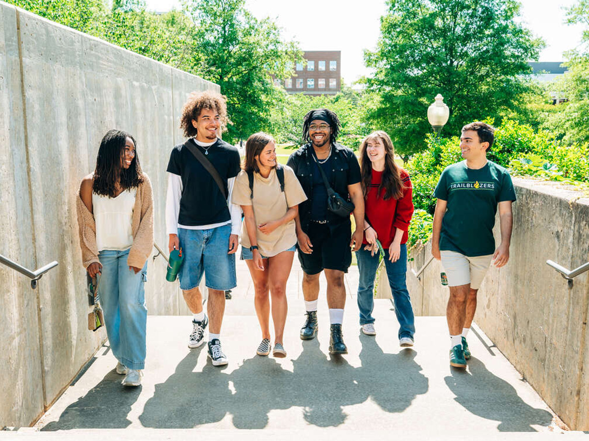 A group of smiling students are walking on a concrete stairway on the Campus Green.