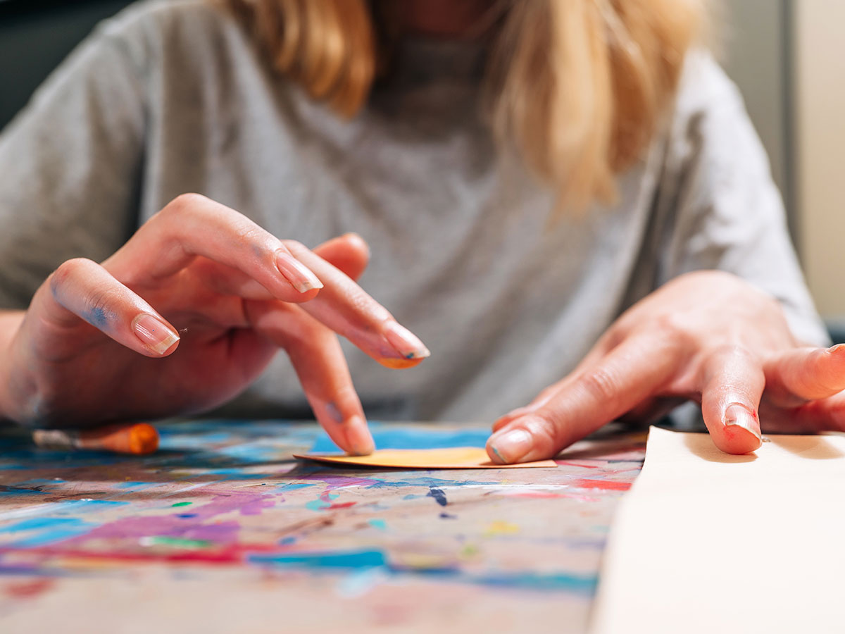Closeup of the hands of a summer camp participant applying color to an artwork