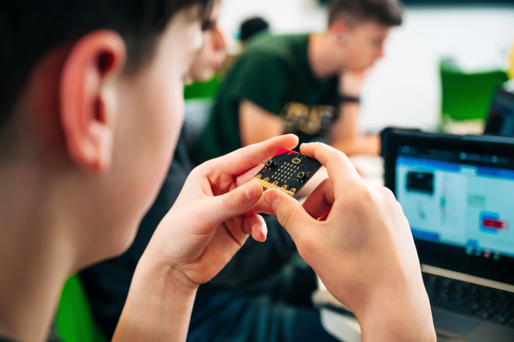 Closeup of student with back to camera holding a small circuit board in a coding camp class