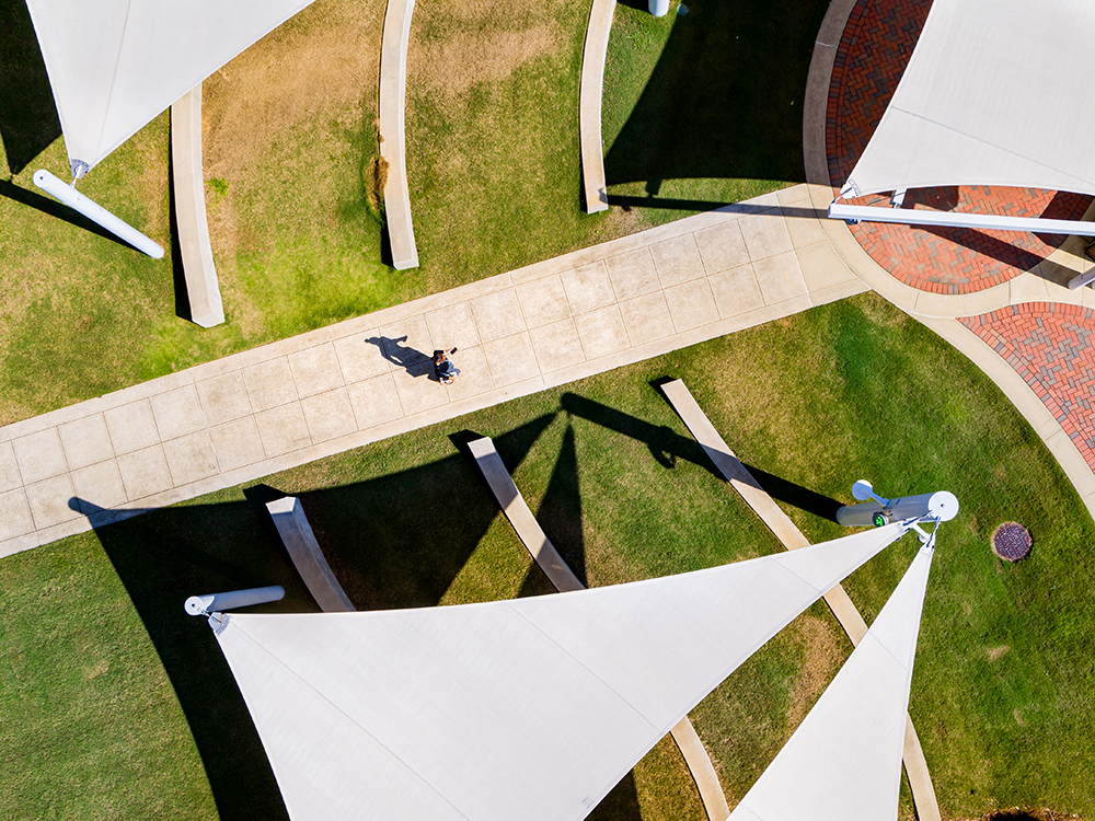 Aerial view of the sail-shaped sunshades over the grassy area in front of the Hill Student Center on U A B's campus, with a lone figure walking on the sidewalk