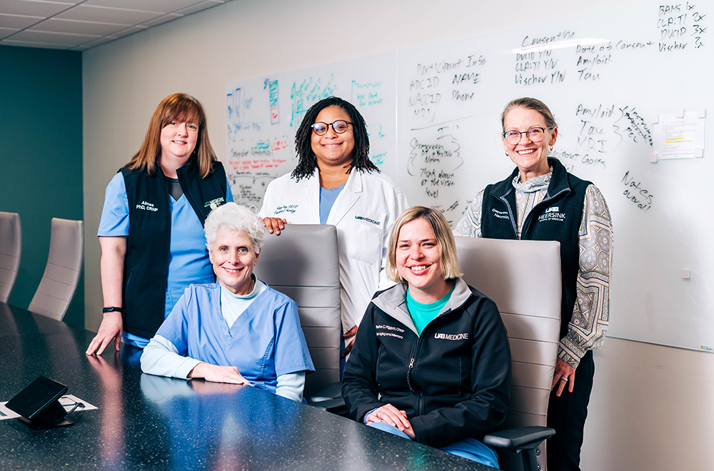 Five nurse practitioners are seated and standing around a conference table in the UAB Brain Aging and Memory Clinic