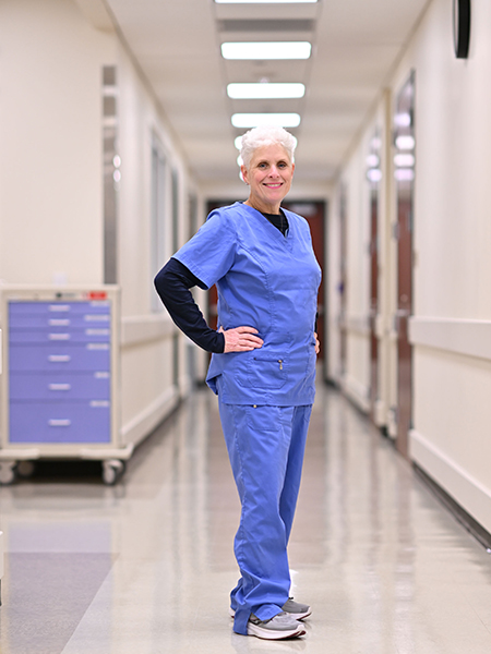 Rita Jablonski, Ph.D., wearing blue scrubs with hands on hips, poses in a hallway of the UAB School of Nursing's simulation suite in this full-length portrait