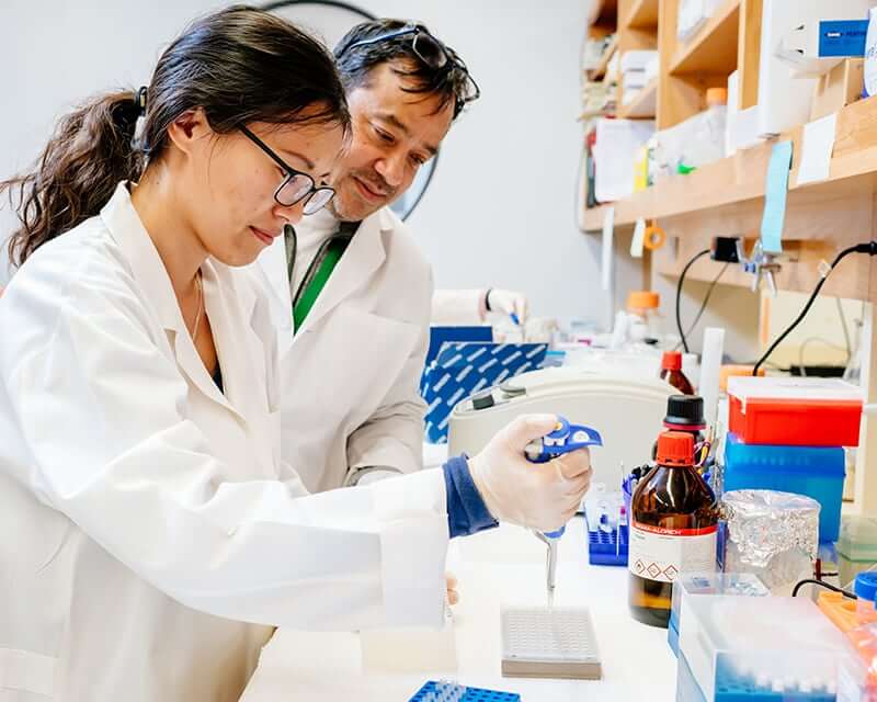 A faculty mentor supervising a female student performing a lab procedure.