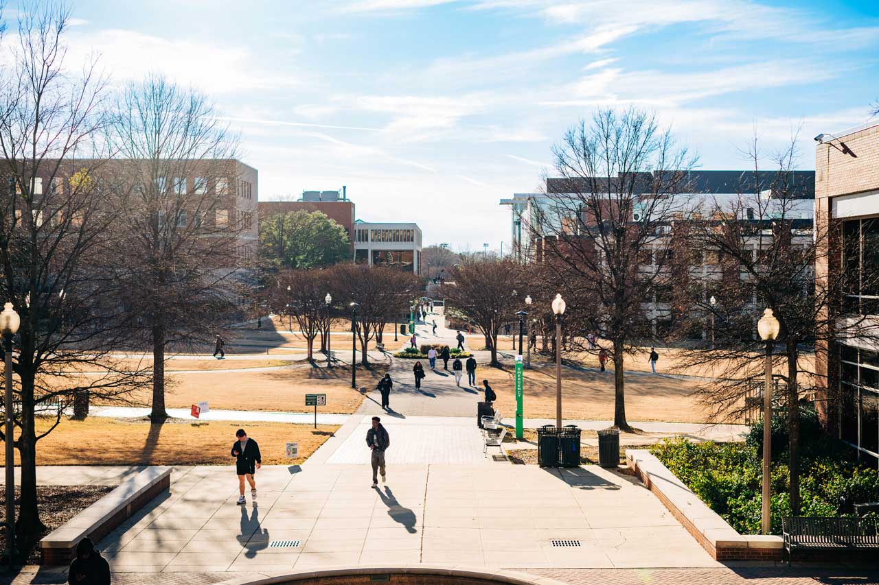 People walk along Campus Green between brick buildings.
