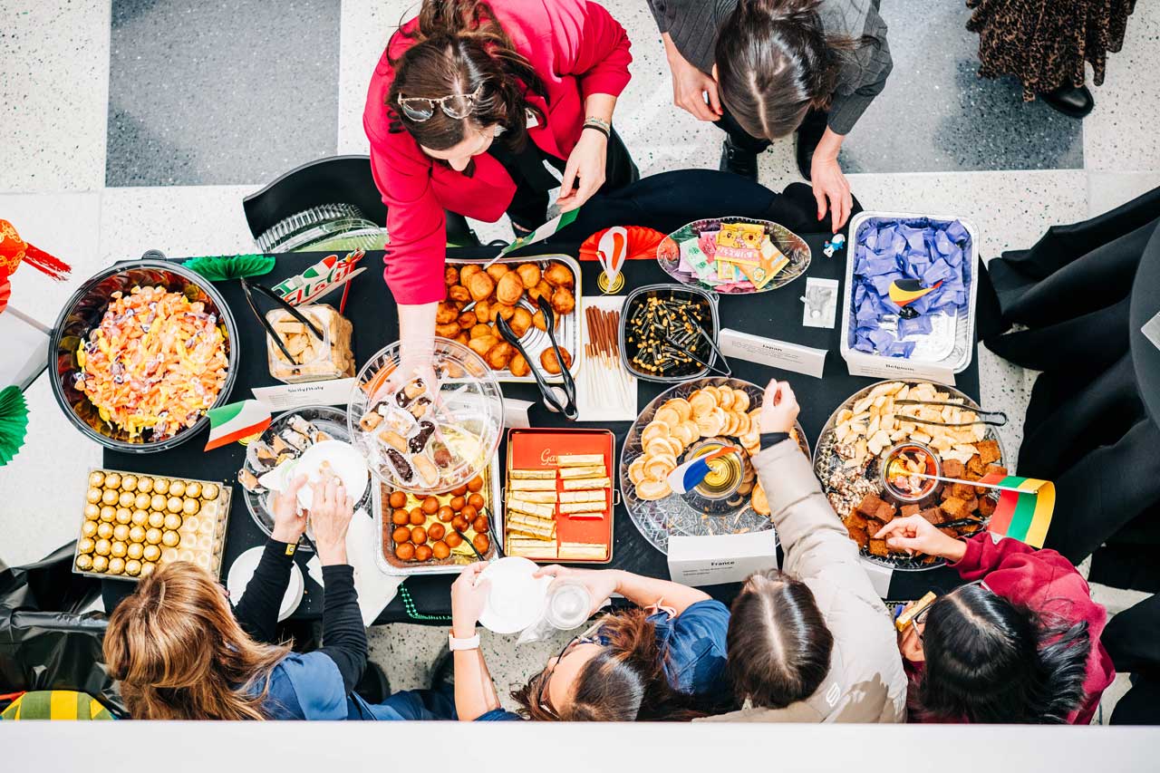 People gather around a table filled with assorted food and snacks.