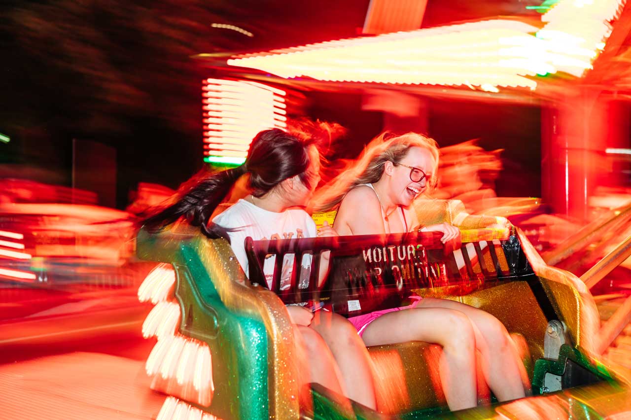 Two people ride a brightly lit carnival ride at night.
